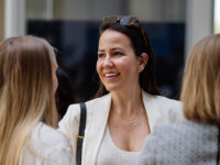 Three women standing in a group. Focus lays on one woman which is looking to the left into the distance. The phot is taken at the Career Day of RWTH Business School