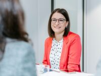 woman in blazer is sitting at the table smiling