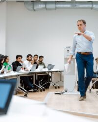 a teacher standing in front of a class of international students and explains something